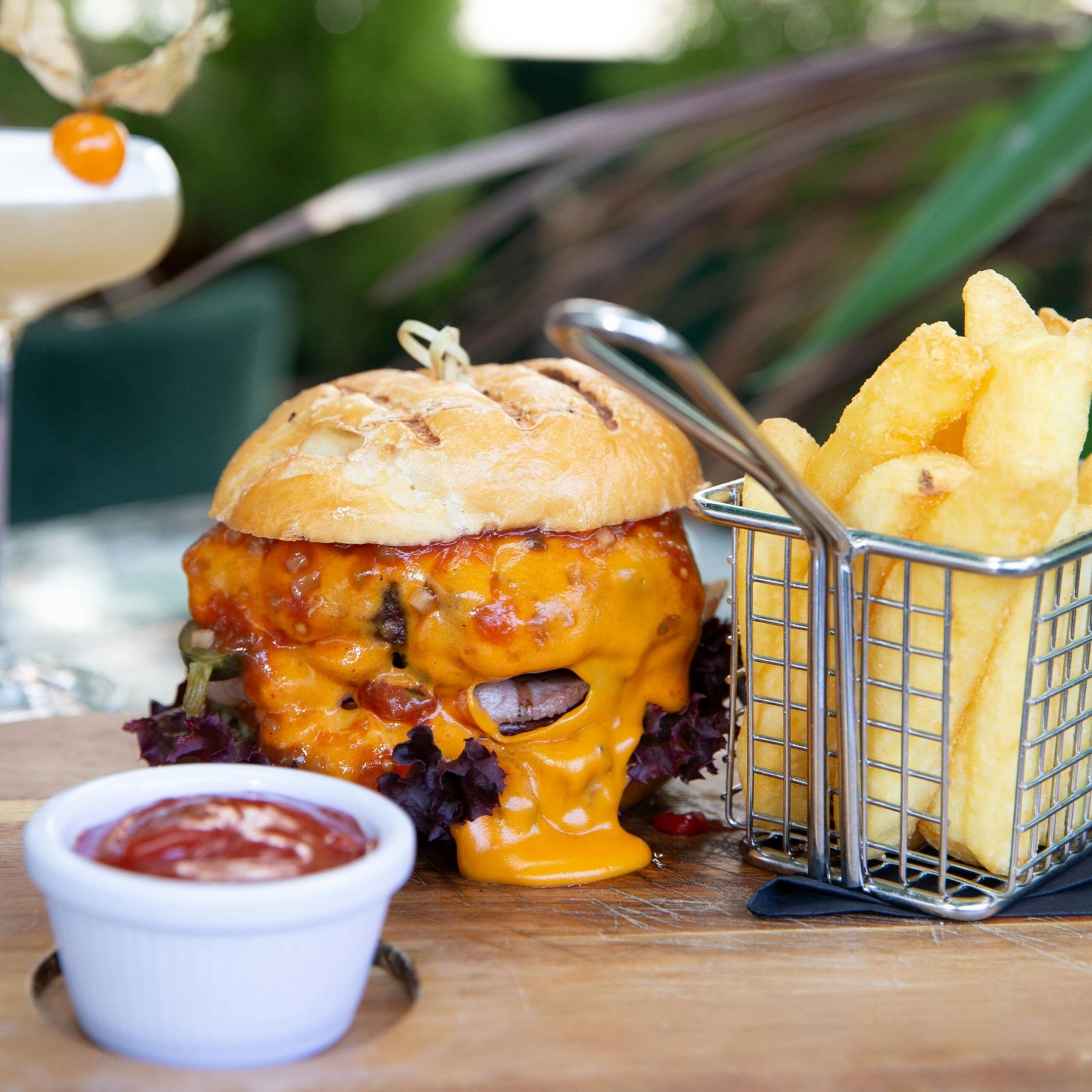 Delicious gourmet cheeseburger served with crispy french fries and dipping sauce on a wooden board.